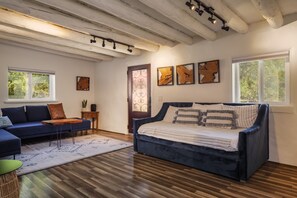 Una sala de estar moderna con un sofá azul, un sofá azul oscuro y piso de madera. Hay tres obras de arte enmarcadas en la pared y una ventana con vista a árboles.