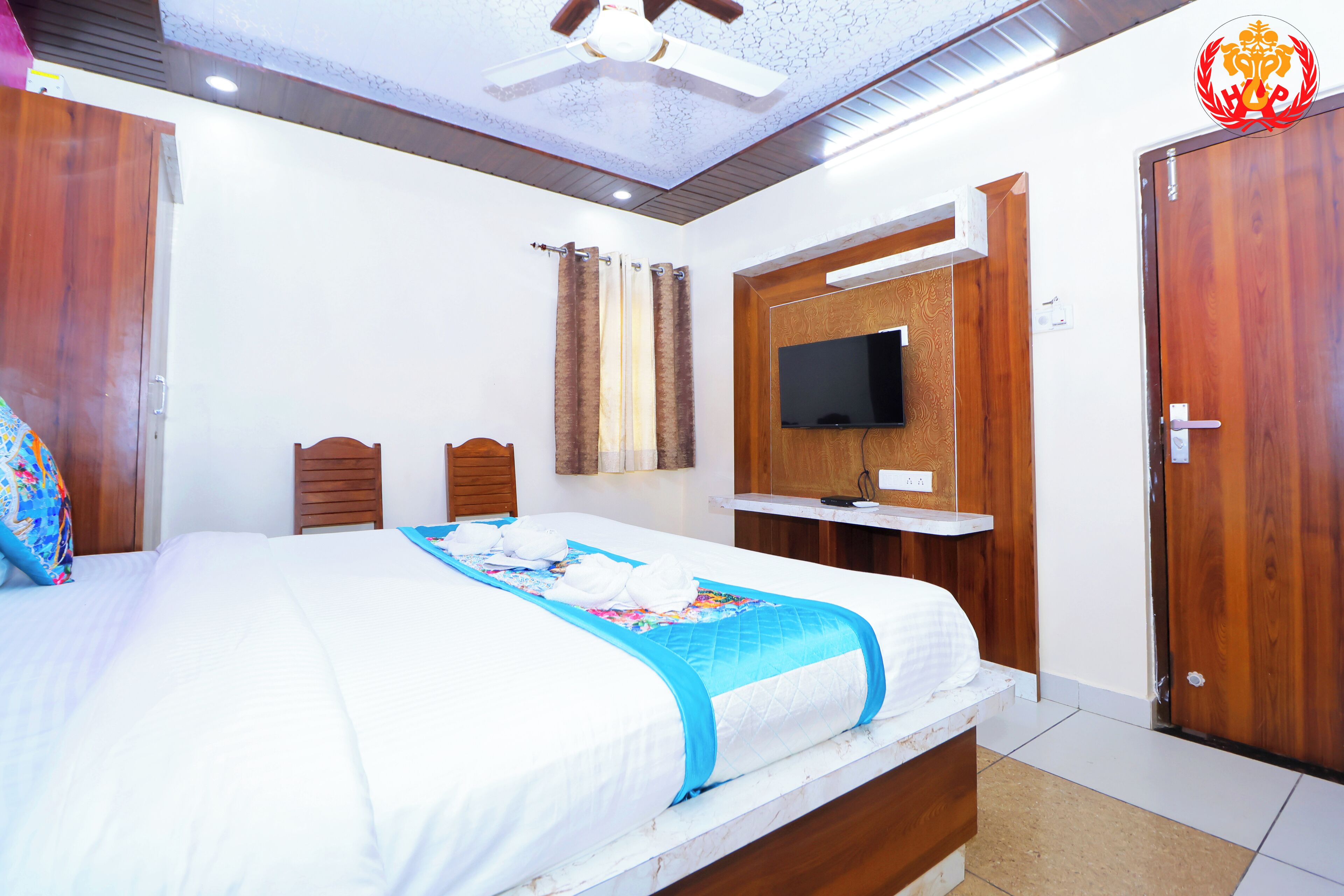 A hotel room with a large bed, wooden headboard, a flat-screen TV mounted on the wall, and a wooden wardrobe.