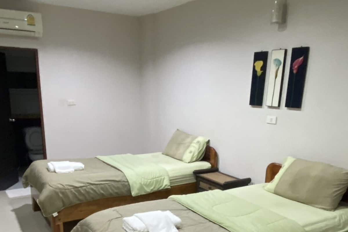 A hotel room with two single beds, a bedside table, a small nightstand, and a wall-mounted air conditioning unit.