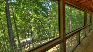Une terrasse en bois avec de grandes fenêtres donnant sur une zone boisée.