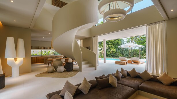 Un salon moderne doté d’un escalier en courbe, d’un grand canapé et offrant une vue sur un espace piscine extérieur.