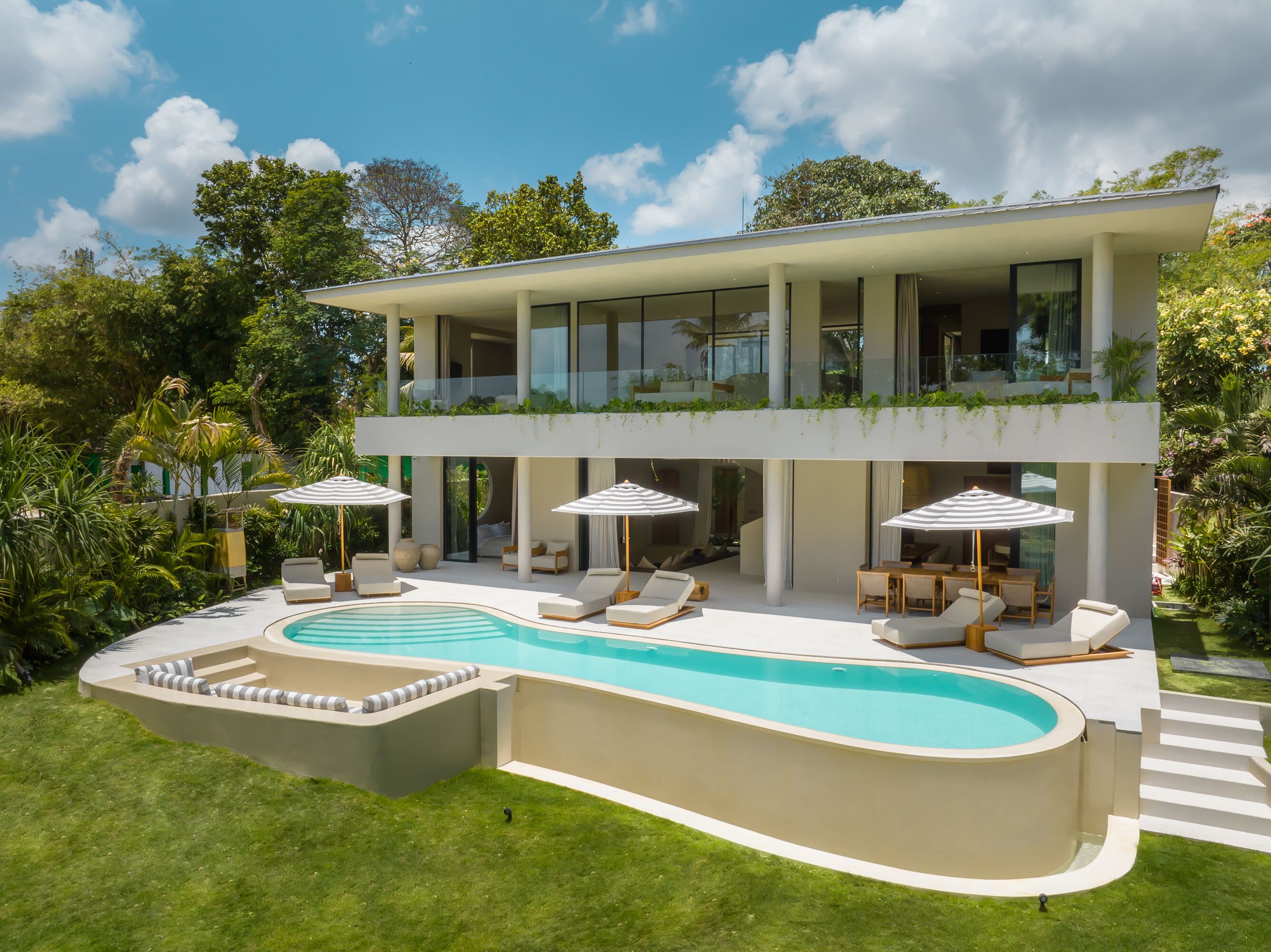 A modern two-story house with a swimming pool, outdoor seating, and lush greenery.