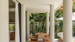 Un espace de vie moderne et ouvert, comprenant un ensemble de canapés en bois, une table à manger avec des chaises et une grande fenêtre donnant sur un jardin.