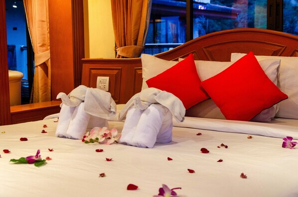 A neatly made bed with white linens, red pillows, and a bouquet of flowers on the bed. - Diva Patong Hotel (Patong)