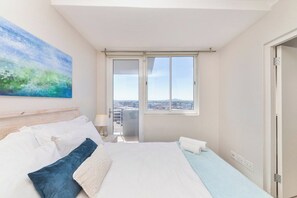 Habitación de hotel con una cama grande, vistas de la ciudad desde un balcón y un cuadro en la pared.