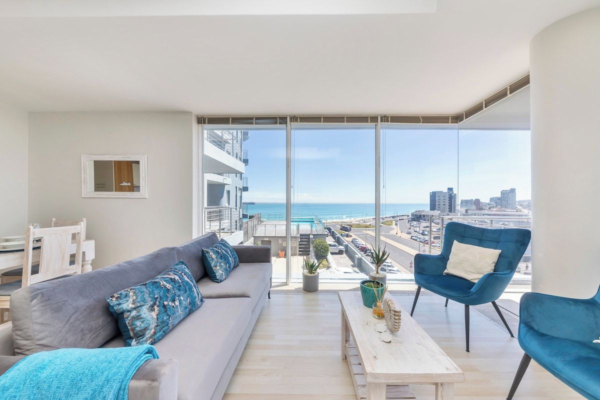 Un balcone con un divano, sedie e un tavolo, vista sulla città e sul mare.