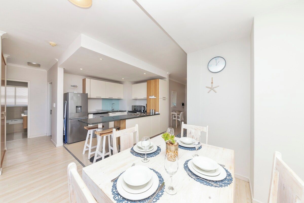 A modern kitchen with white cabinets, a central island, and a dining area with a white table set for four.