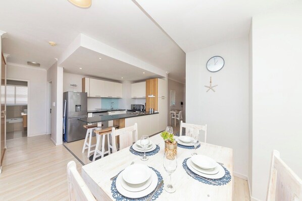 A modern kitchen with white cabinets, a central island, and a dining area with a white table set for four.