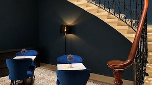 A curved staircase with a wooden handrail and black balusters, leading to a landing with two blue chairs and a small table. - Mulberry Suites by The LVH Collection  (Valletta)