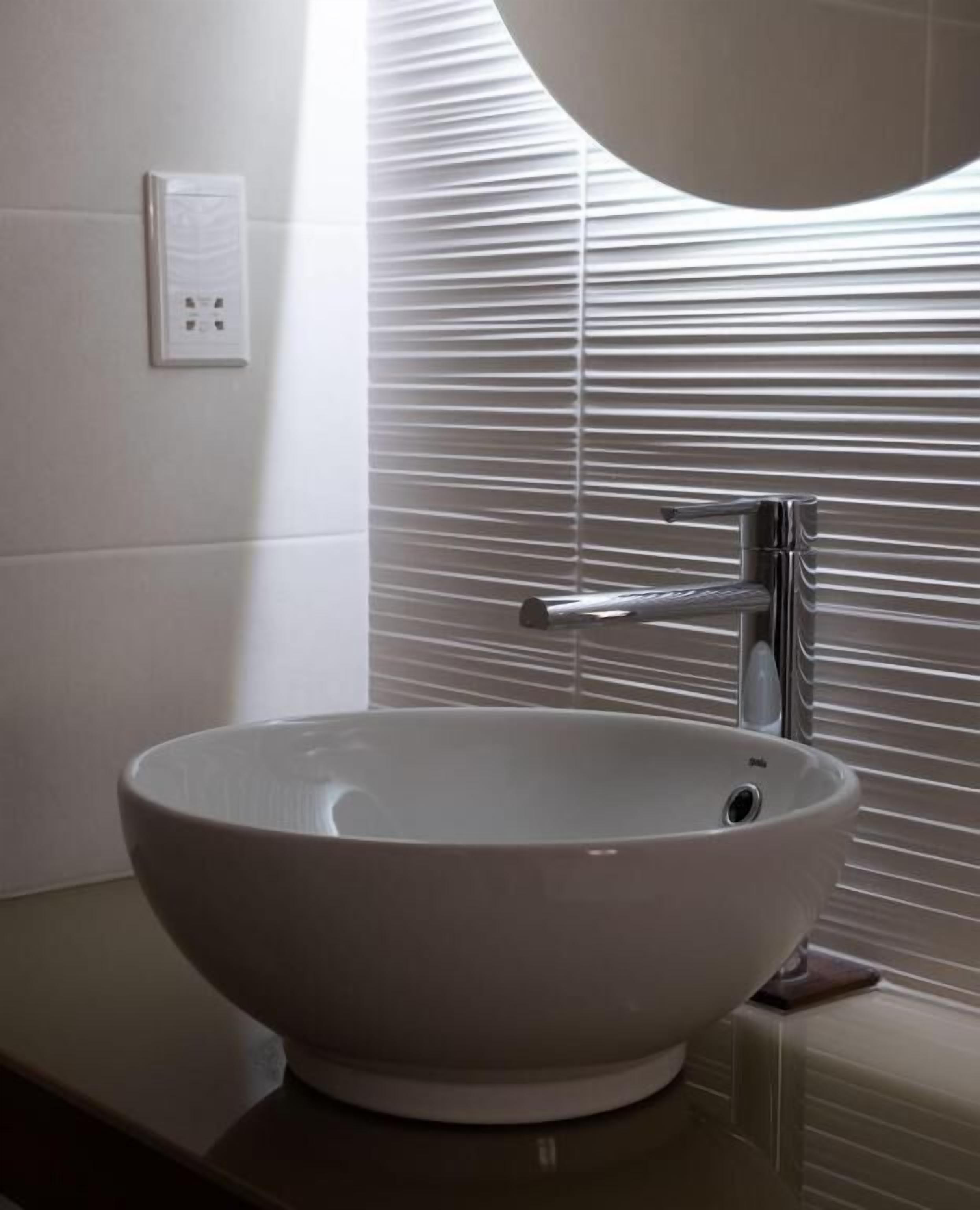 Un baño con un lavamanos blanco tipo recipiente, una grifería moderna y una ventana con persianas.