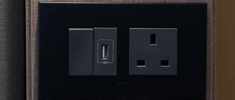 Un enchufe eléctrico negro con un puerto USB y un enchufe estándar de dos clavijas en una pared con textura.