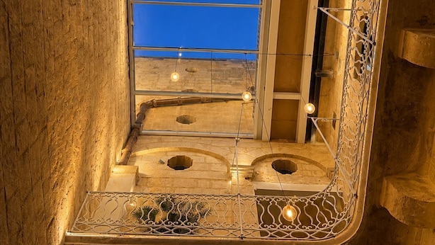 A bathroom with a unique architectural design, featuring a large window, a small sink, and decorative lighting. - Mulberry Suites by The LVH Collection  (Valletta)