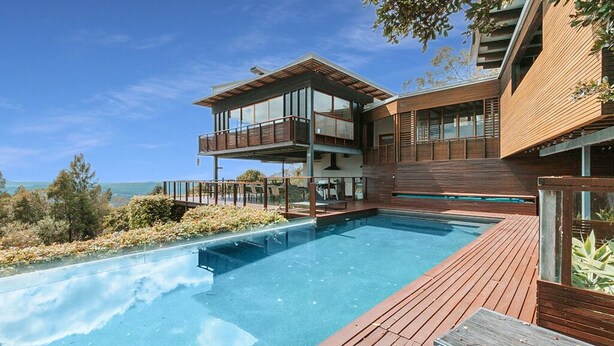 A modern house with a large swimming pool, wooden deck, and a second-story balcony.