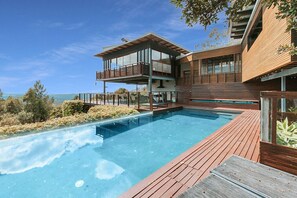 Ein modernes Haus mit großem Schwimmbad, Holzterrasse und einem Balkon im zweiten Stock.
