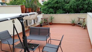 A rooftop terrace with a table and four chairs, surrounded by potted plants and a view of greenery. - Historical center apartment.(Nina's house Venice) (Palermo)