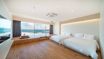 A modern hotel room with two beds, a wooden floor, a large window with a view of the sea, and a balcony.