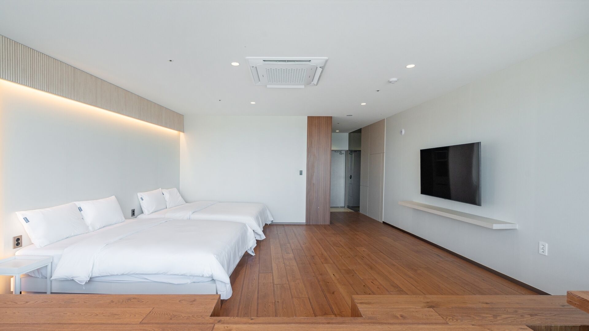 Una habitación de hotel moderna con una cama grande, un televisor montado en la pared y piso de madera.