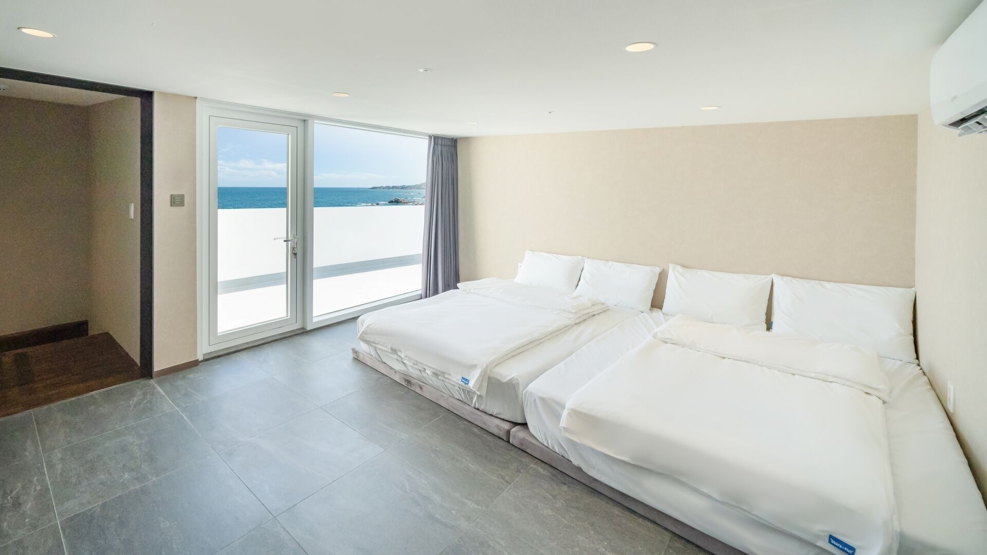 A hotel room with a large bed, a sliding glass door leading to a balcony, and a view of the sea.