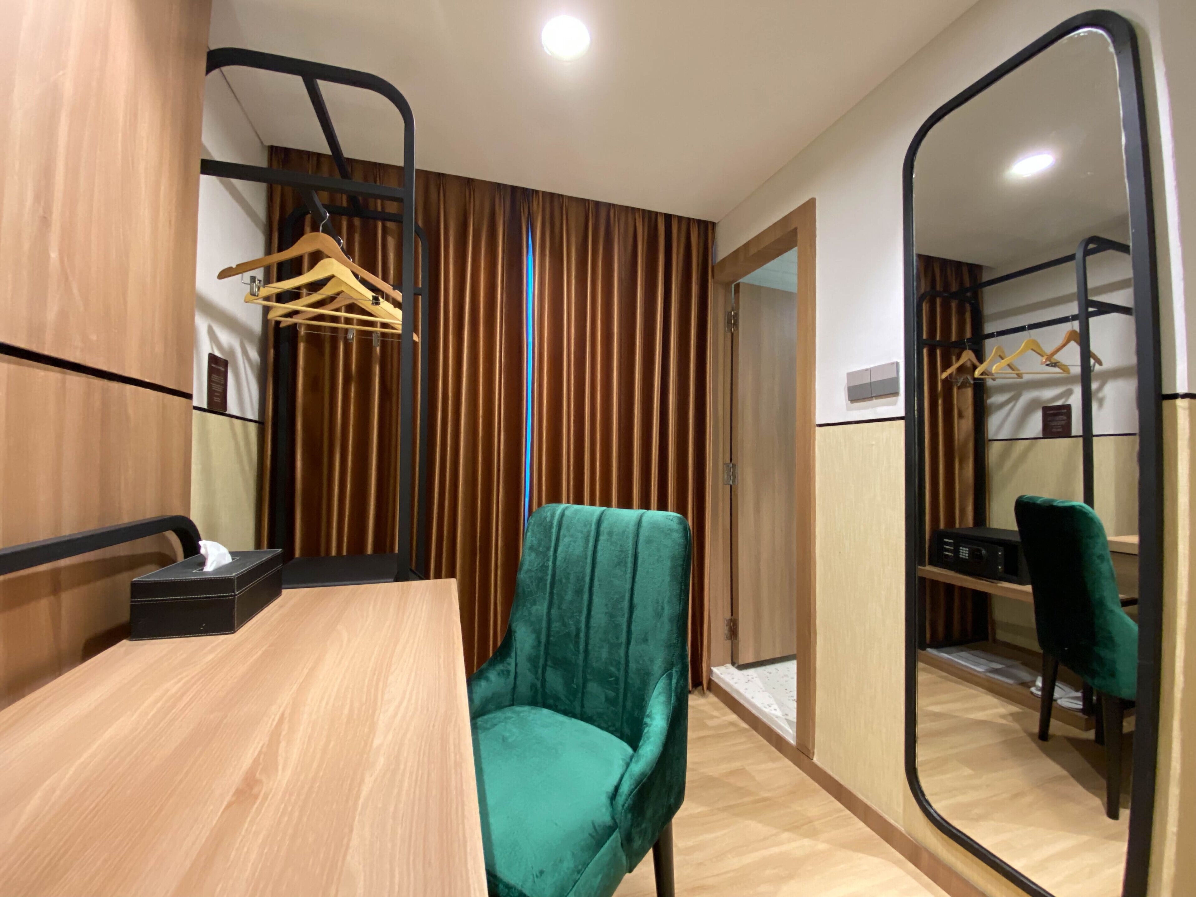 Una habitación moderna con una mesa de madera, una silla color turquesa, un espejo y un armario con perchero.