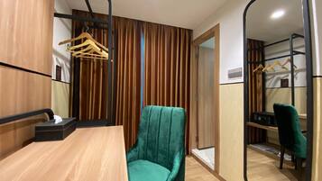 Una habitación moderna con una mesa de madera, una silla color turquesa, un espejo y un armario con perchero.