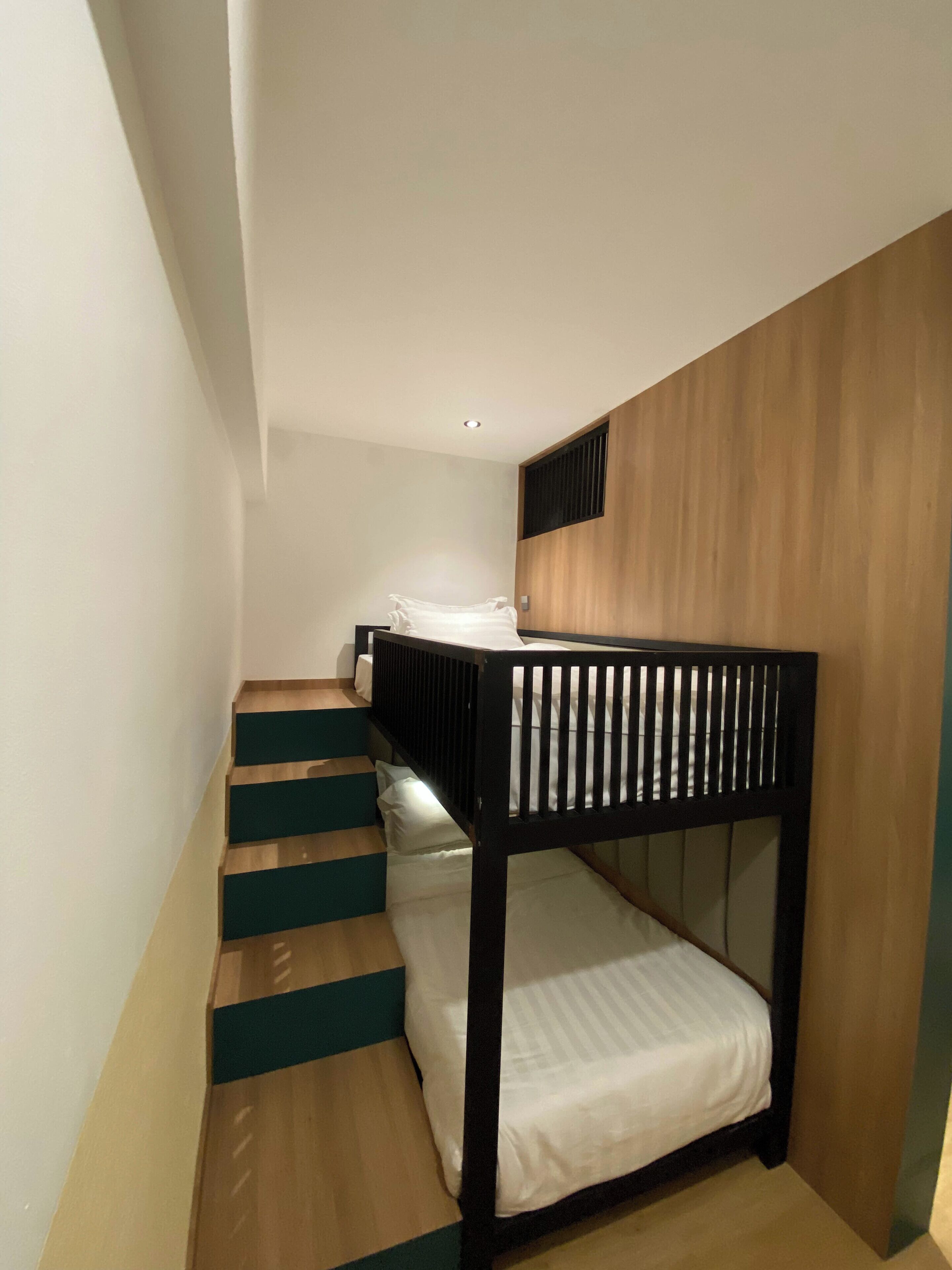 A bunk bed with a wooden headboard and a staircase with teal steps leading to a landing.