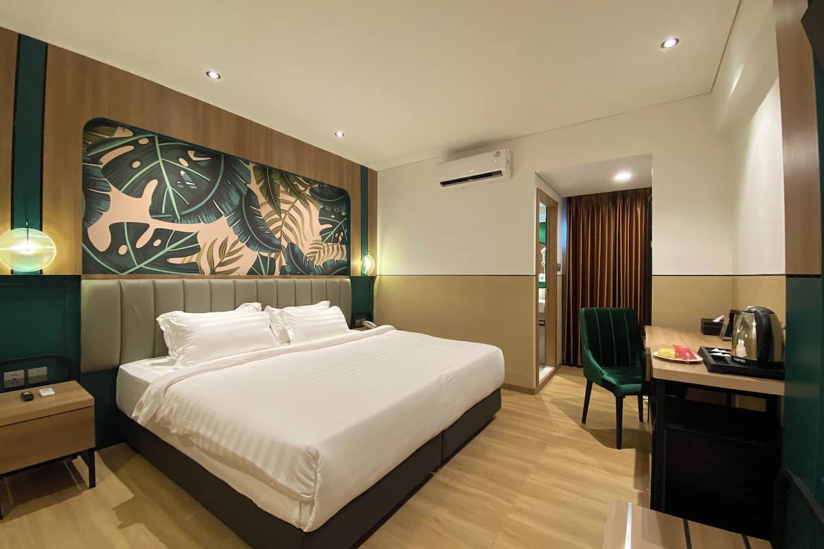 Una habitación de hotel moderna con una cama grande, un escritorio con una silla, un aire acondicionado de pared y un papel tapiz con diseño de hojas.