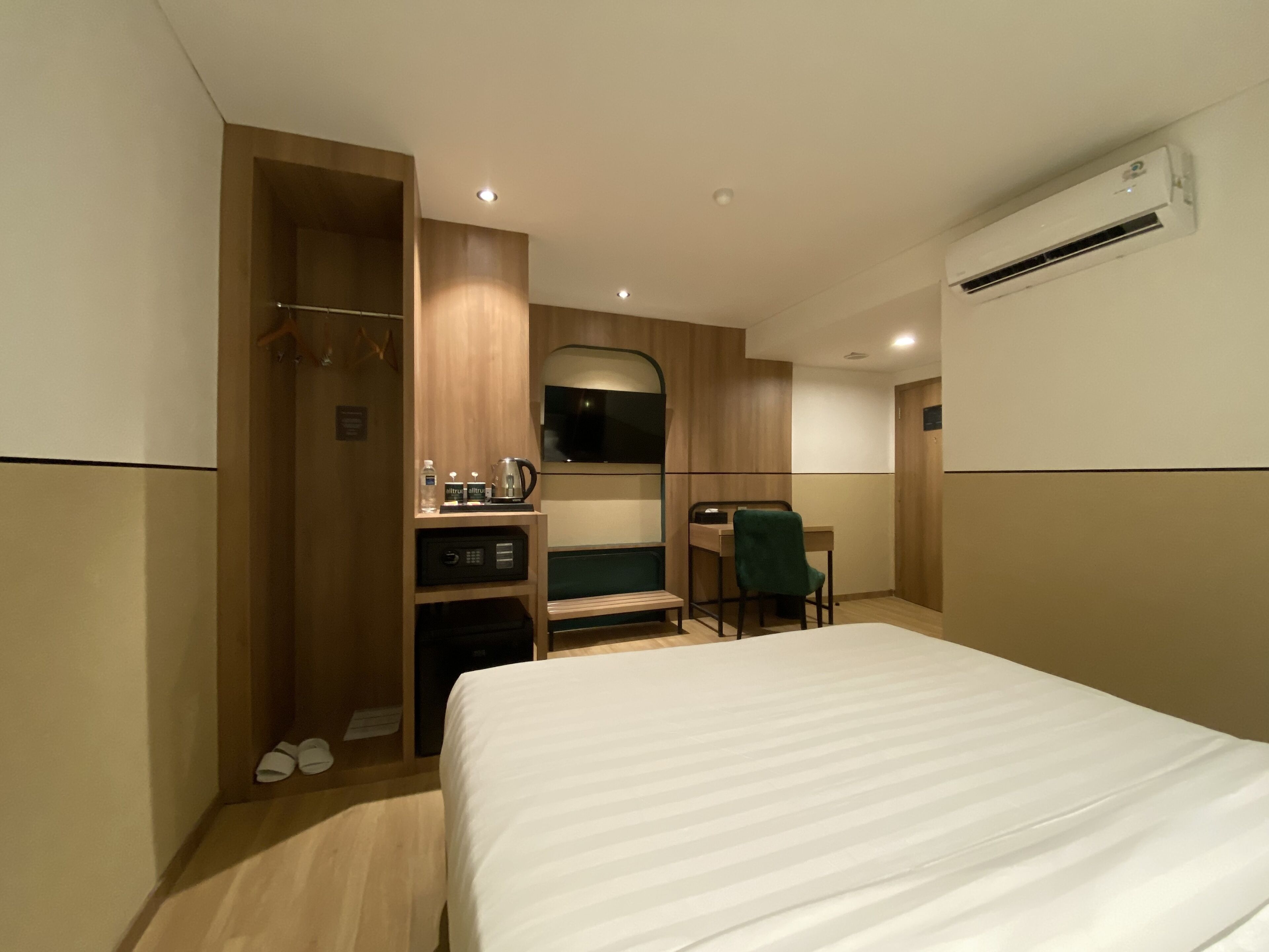 Habitación de hotel con cama, escritorio, silla, armario y unidad de aire acondicionado.