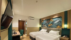 Habitación de hotel con dos camas, un escritorio, una silla, un televisor y una pared con diseño de hojas.