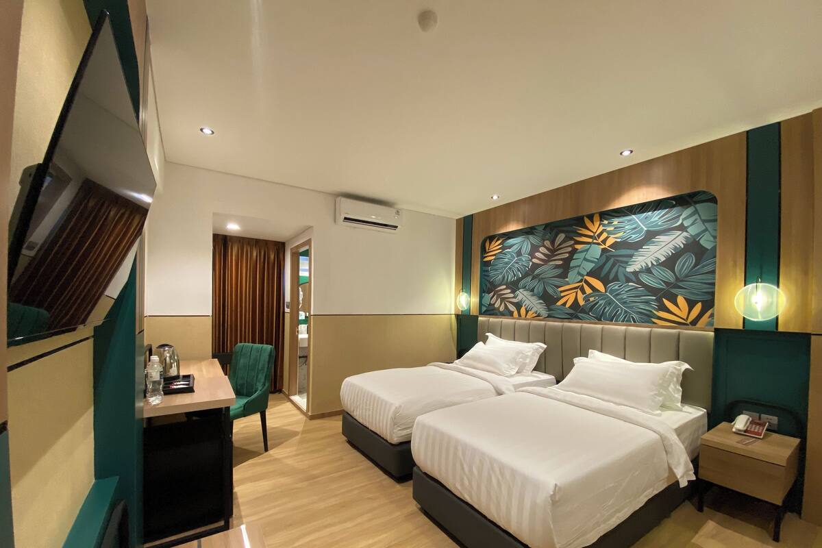 Habitación de hotel con dos camas, un escritorio, una silla, un televisor y una pared con diseño de hojas.