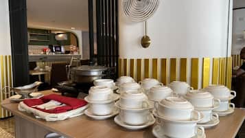 A dining area with multiple white teapots and cups arranged on a wooden table, with a kitchen visible in the background.