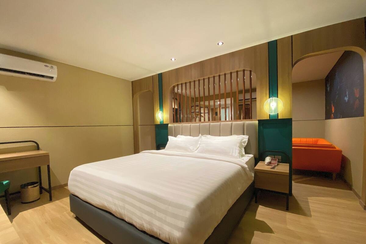 Una habitación de hotel moderna con una cama grande, una mesita de noche con teléfono y una pequeña zona de estar anaranjada.