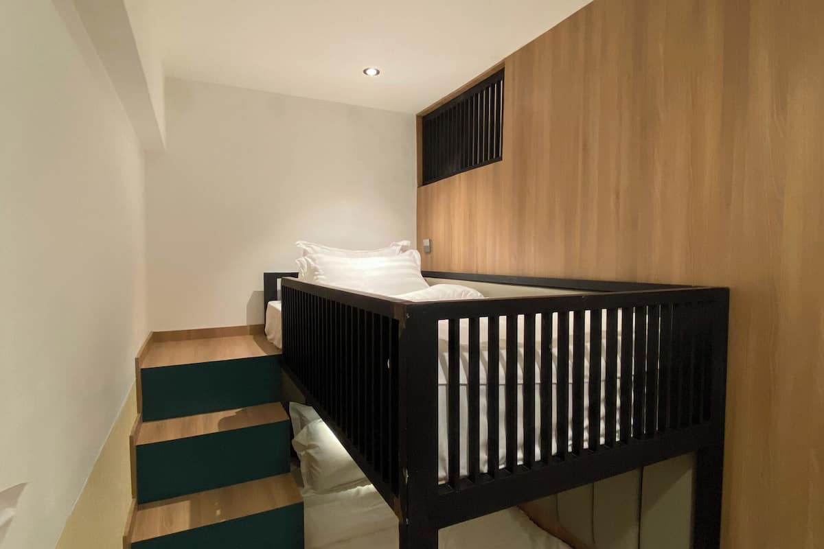 Una cama individual con cabecera de madera y escalera con peldaños claros y oscuros alternados.