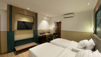 A hotel room with two beds, a desk with a chair, a bench, a TV, and an air conditioning unit.