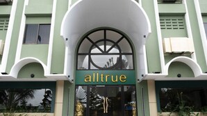 Un edificio con fachada verde, una amplia entrada en arco y el nombre 'alltrue' sobre las puertas.