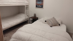 A room with two bunk beds, a small table with a lamp, and a poster on the wall.