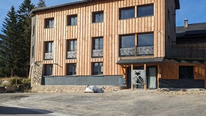 A modern wooden building with multiple windows and balconies, stone foundation, and a gravel driveway.