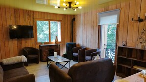 A cozy room with wooden walls, a flat-screen TV, a fireplace, and comfortable seating.