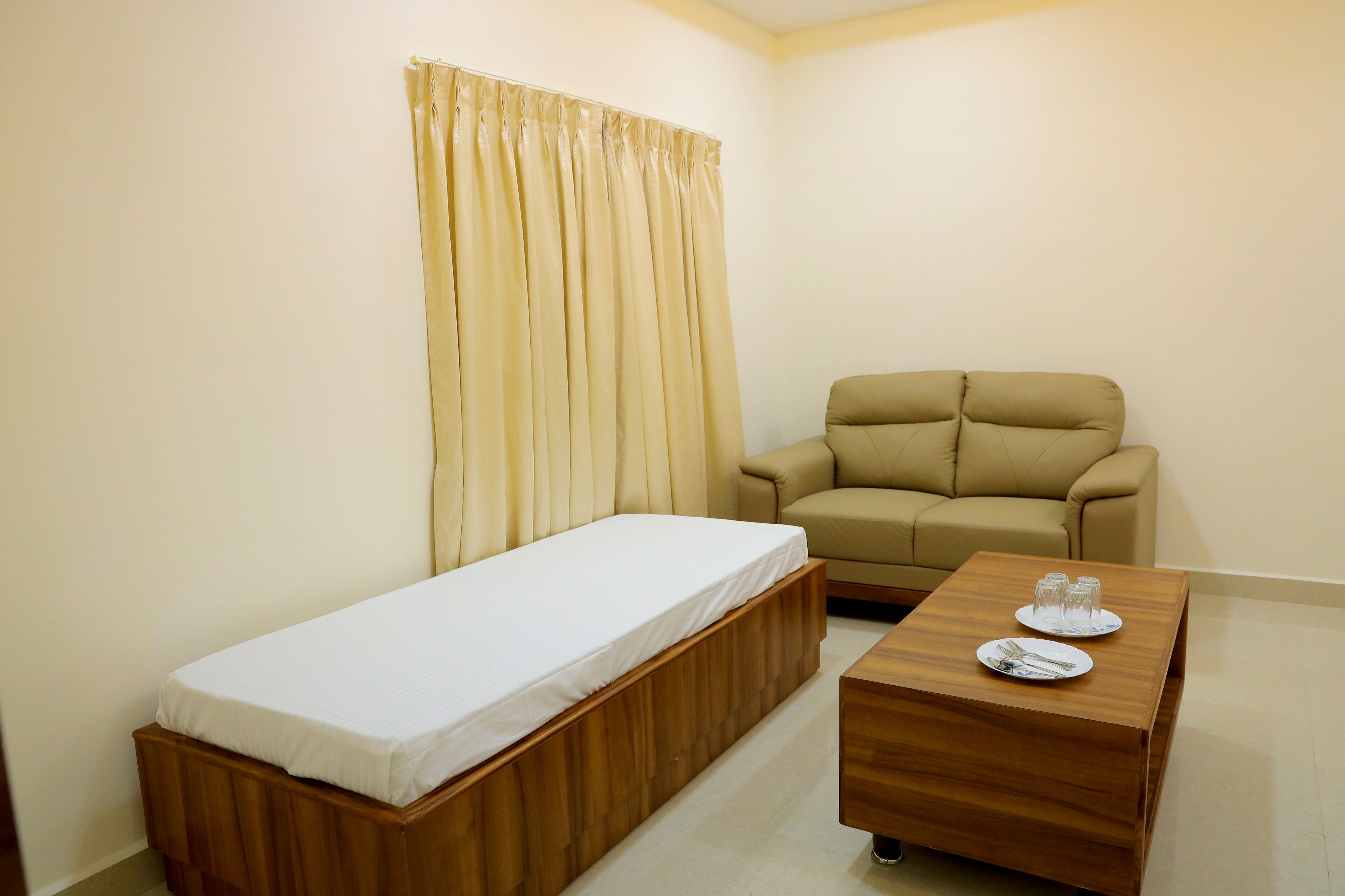 A small room with a single bed, a sofa, and a wooden coffee table with a plate and glasses on it.