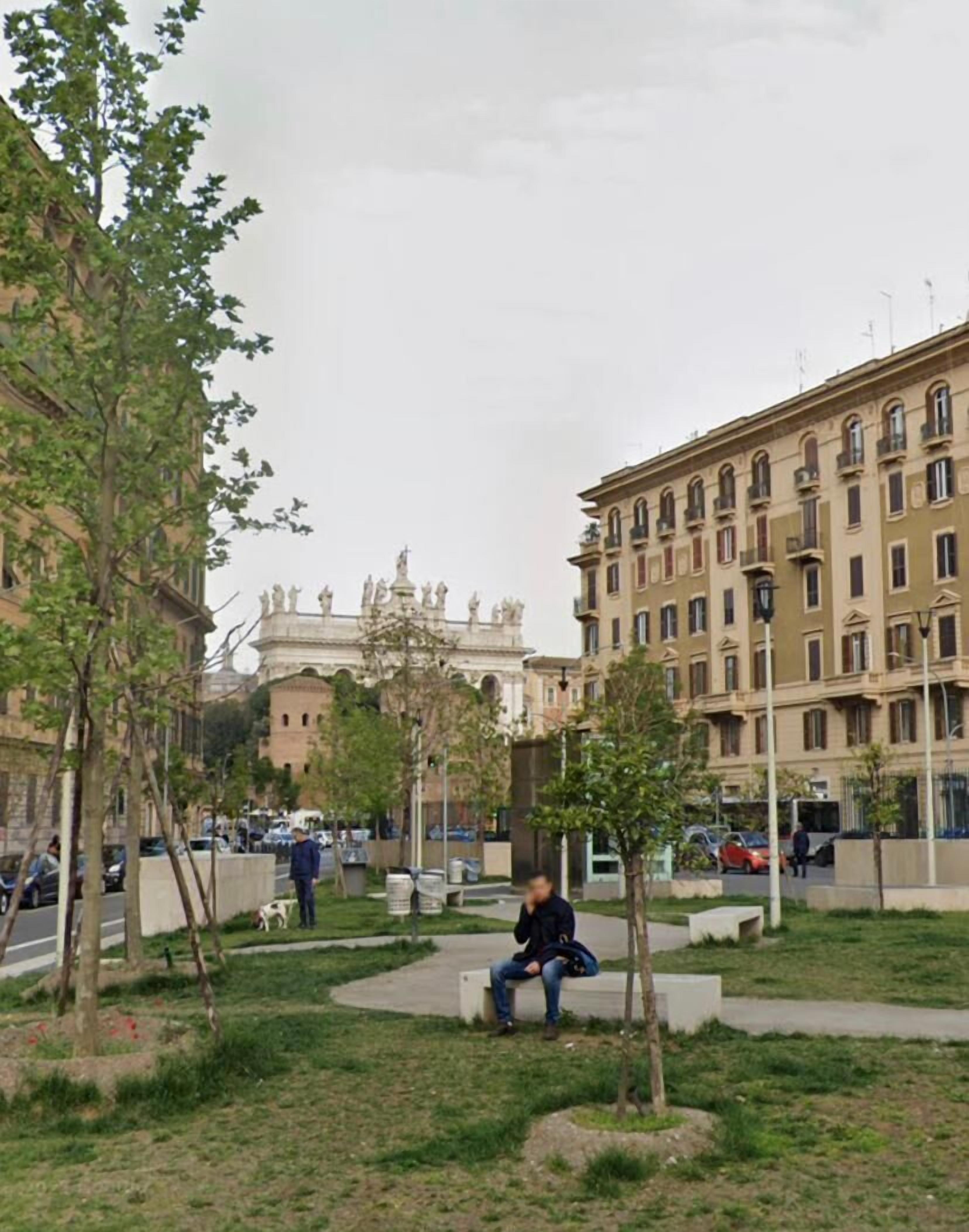 A park with a bench, trees, and a building with classical architecture in the background.