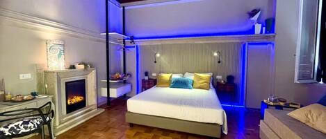 Un dormitorio moderno con chimenea, una cama con muchas almohadas, un escritorio con silla y una lámpara colgante.