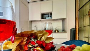Una mesa de comedor con una variedad de frutas y verduras, un vaso de líquido rojo y una bolsa de papel con chiles rojos.