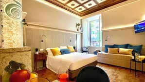 Una habitación de hotel con cama, sofá, televisor y una mesa de comedor con fruta y una copa de vino.