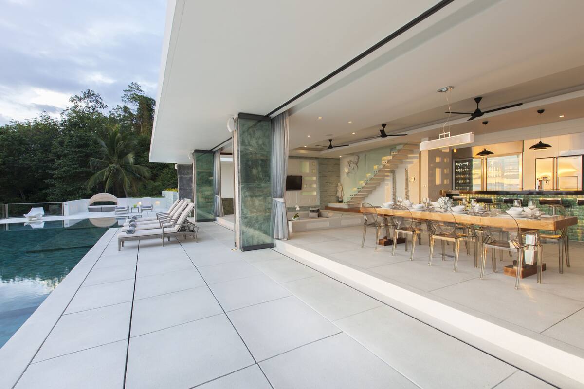 A modern outdoor dining area with a pool, lounge chairs, and a staircase leading to an upper level.