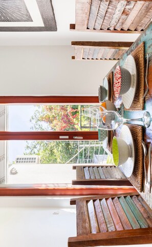 A dining area with a wooden table and chairs, a glass wine glass, and a view of trees and buildings outside.