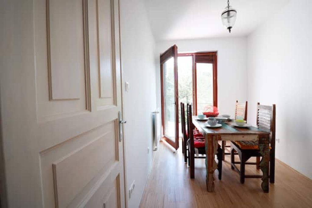 Een eetruimte met een houten tafel en stoelen, een groot raam en een deur met een ruit.