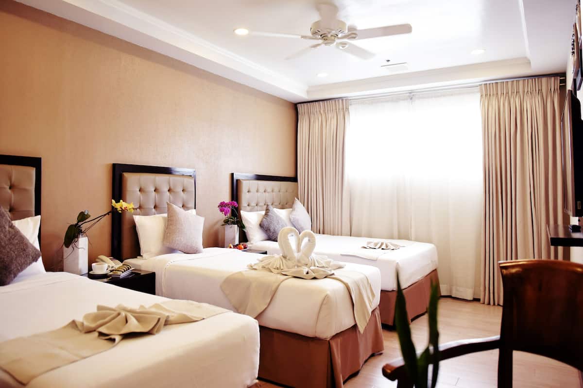 A hotel room with two beds, a ceiling fan, and a large window with curtains.