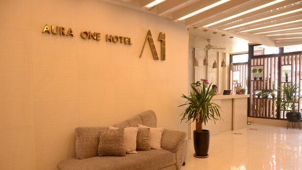 A reception area with a sofa, a potted plant, and a sign for "AURA ONE HOTEL". - Aura One Hotel (Baguio)