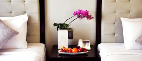 A hotel room with two beds, a nightstand with a vase of flowers, and a framed artwork on the wall.
