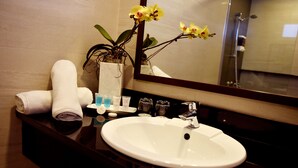A bathroom with a white sink, a mirror, and a vase with yellow flowers. - Aura One Hotel (Baguio)
