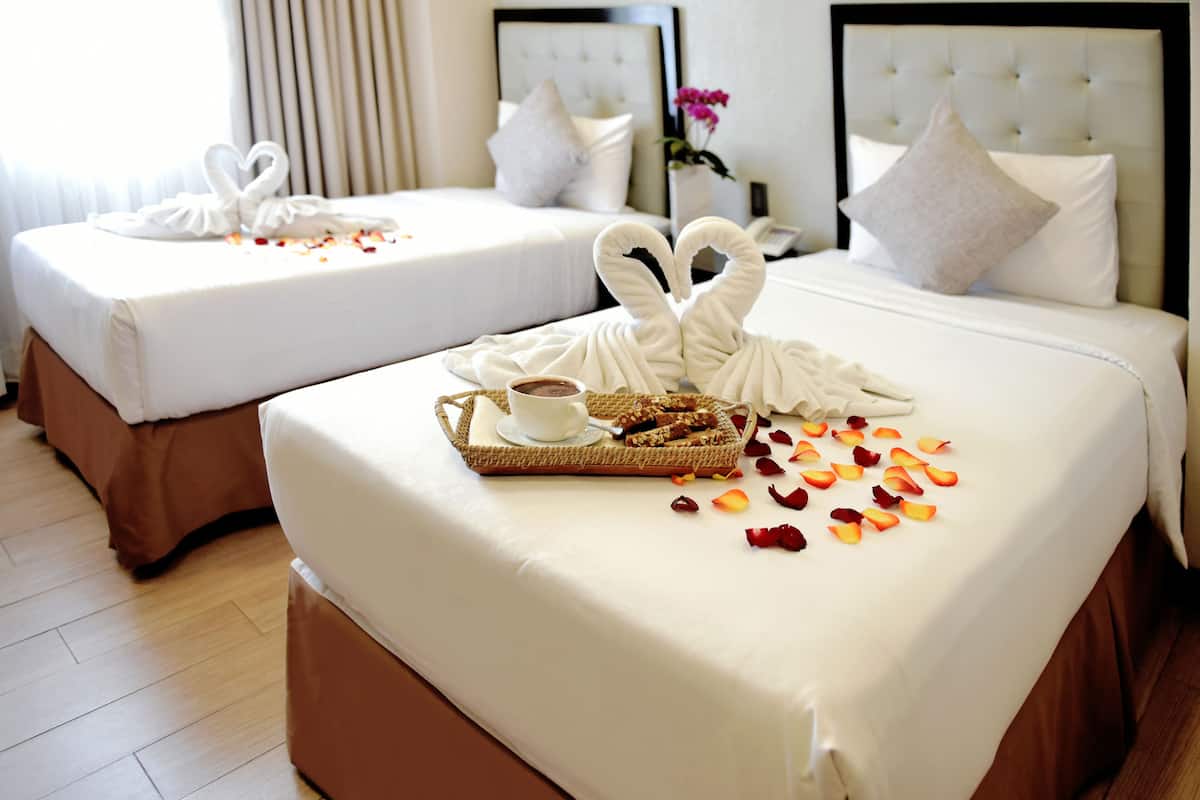 Two neatly made beds with white linens, a tray with a cup and pastries, and rose petals scattered on the bed.